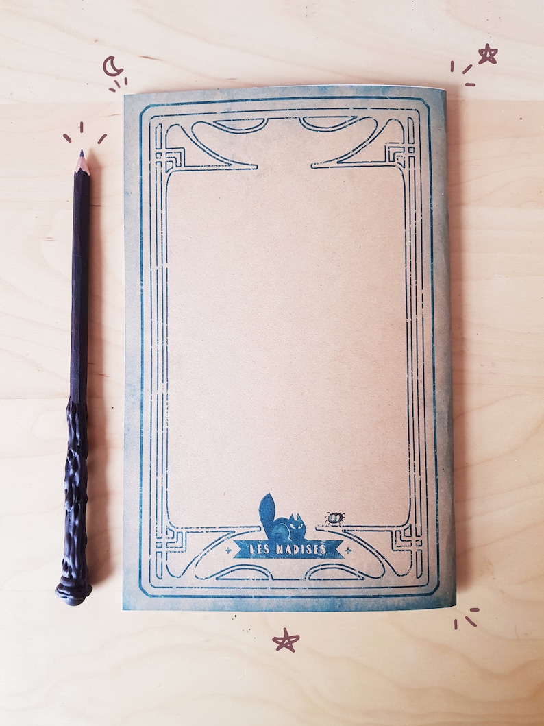 May include: A brown notebook with a blue decorative border and a small illustration of a cat and a bug. The notebook has the text "LES NADISES" printed on the bottom.