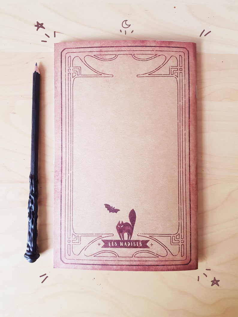 May include: A brown notebook with a decorative border and a black cat and bat illustration. The notebook has the text "LES NADISES" printed on the front.