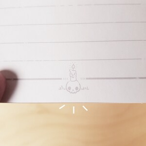 May include: A white lined notebook with a small gray skull and candle illustration at the bottom of the page.