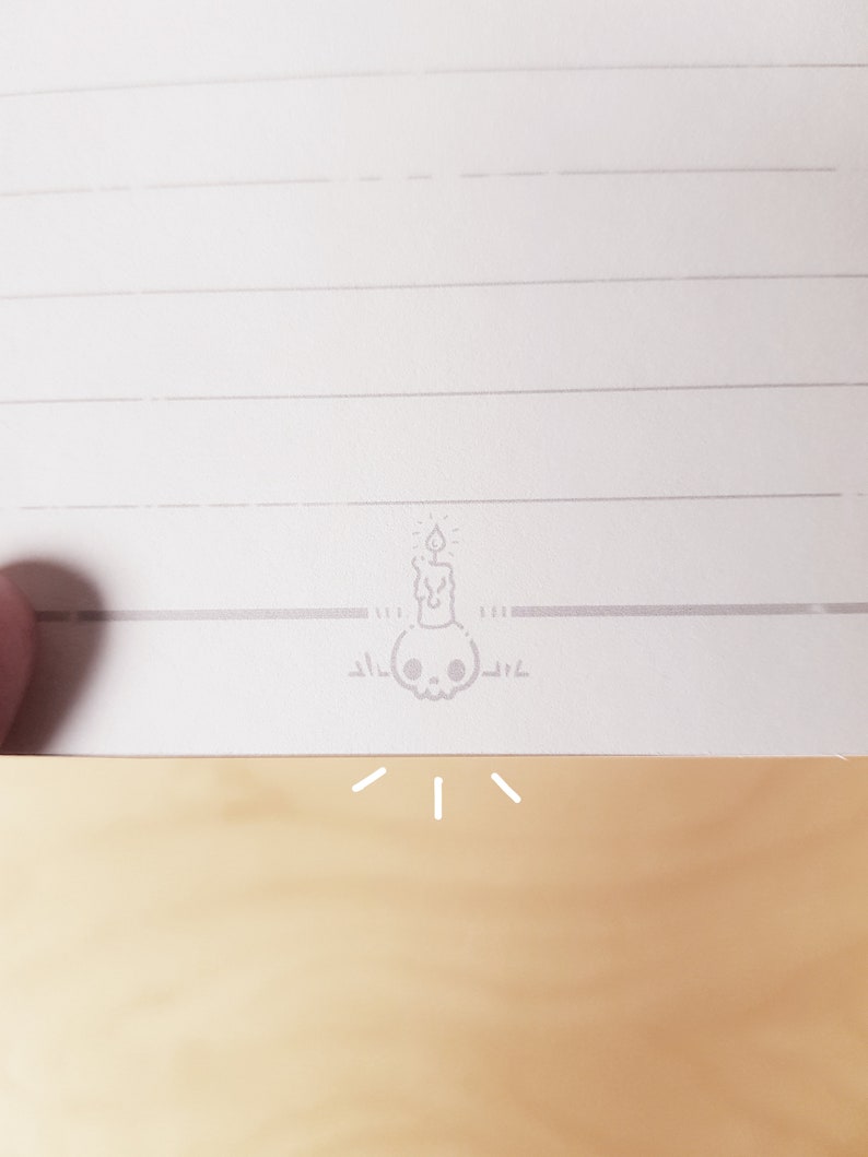 May include: A white lined notebook with a small gray skull and candle illustration at the bottom of the page.