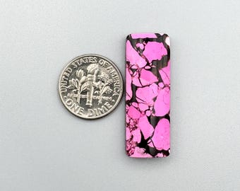 May include: A pink and black cabochon gemstone with a marbled pattern. The gemstone is approximately the size of a US dime.