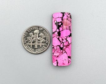 May include: A pink and black cabochon gemstone with a marbled pattern. The gemstone is about the size of a US dime.