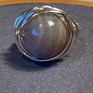 May include: A silver wire wrapped ring with a round, gray gemstone.