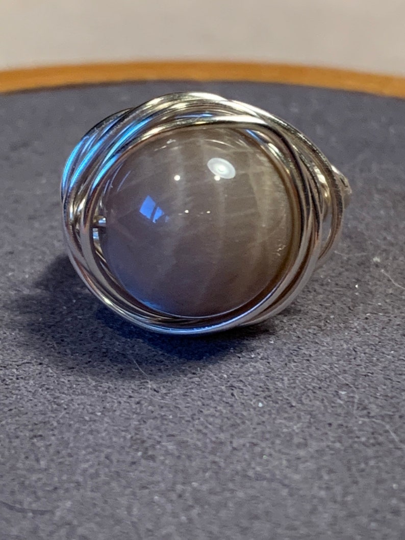 May include: A silver wire wrapped ring with a round, gray gemstone.