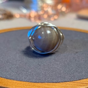 May include: A silver wire wrapped ring with a round, light gray stone.