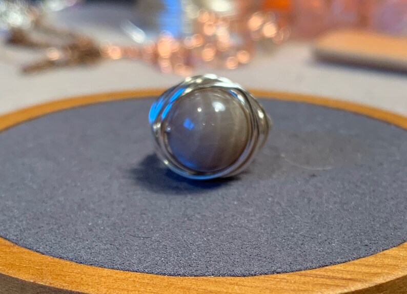 May include: A silver wire wrapped ring with a round, light gray stone.