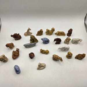 Peut inclure: Une collection de vingt-trois petites figurines d'animaux en céramique émaillée, aux poses et couleurs variées, incluant des tons de brun, beige, blanc et bleu. L'ensemble représente divers animaux comme des ours, oiseaux et lapins.