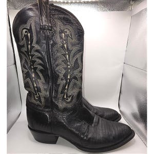 Può includere: Uno stivale da cowboy in pelle nera con finitura testurizzata sul piede e un gambale alto con intricate cuciture decorative di colore chiaro. Lo stivale presenta una punta affusolata, un tacco a blocco e linguette sul bordo superiore.