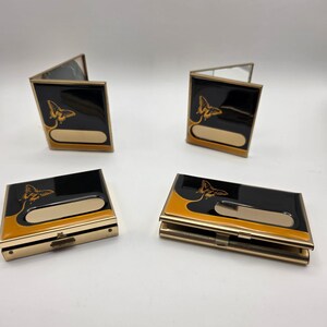 以下が含まれることがあります： 蝶のデザインが施された、黒と金のビジネスカードホルダー4つ。ホルダーは長方形で、金のトリムと名前用の金色の長方形のスペースがあります。蝶は金色です。