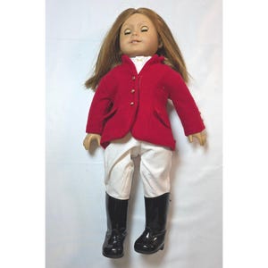 May include: A doll with long brown hair and closed eyes wearing a red equestrian-style jacket with gold-tone buttons, a white collared shirt underneath, white riding breeches, and black shiny knee-high boots. The doll has a neutral facial expression.