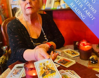 May include: A woman performs a tarot card reading, holding up a card with a golden chalice design. The card is part of a spread of tarot cards on a table with a lit candle and other decorative items. The text on the sign above the woman reads "Two Questions Career Tarot Reading".
