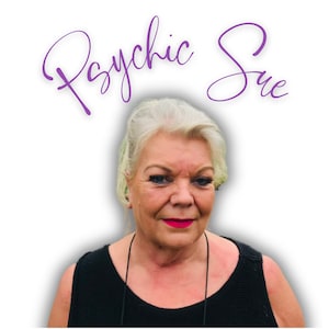 May include: A woman with white hair and red lipstick is smiling at the camera. The text "Psychic Sue" is written in purple cursive above her head.
