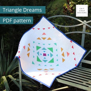 May include: A white quilt featuring a geometric pattern of small triangles in shades of red, orange, yellow, green, teal, and purple, with a blue border. The text Triangle Dreams PDF pattern and Cait Lisle Designs are visible.