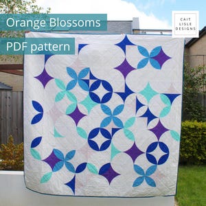 May include: A quilt featuring a white background with a geometric pattern of interlocking circles and four-pointed stars in shades of blue, teal, and purple. The text "Orange Blossoms PDF pattern" and "CAIT LISLE DESIGNS" is visible on the image.