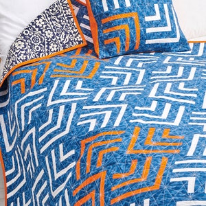 May include: A blue and white quilt with orange geometric patterns. The quilt is made with a variety of fabrics and has a modern design.