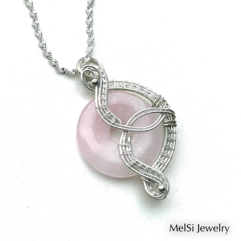 May include: A silver wire wrapped pendant featuring a pale pink rose quartz stone. The pendant is attached to a silver chain.