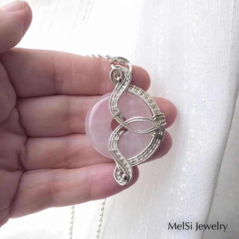 May include: A silver wire wrapped pendant featuring a light pink rose quartz stone. The pendant is shaped like a figure eight and hangs from a silver chain.