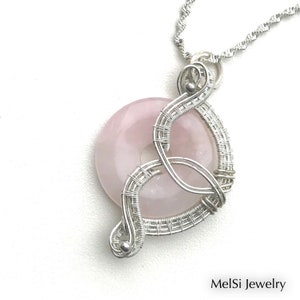 May include: A silver wire wrapped pendant featuring a pink rose quartz stone. The pendant is attached to a silver chain.