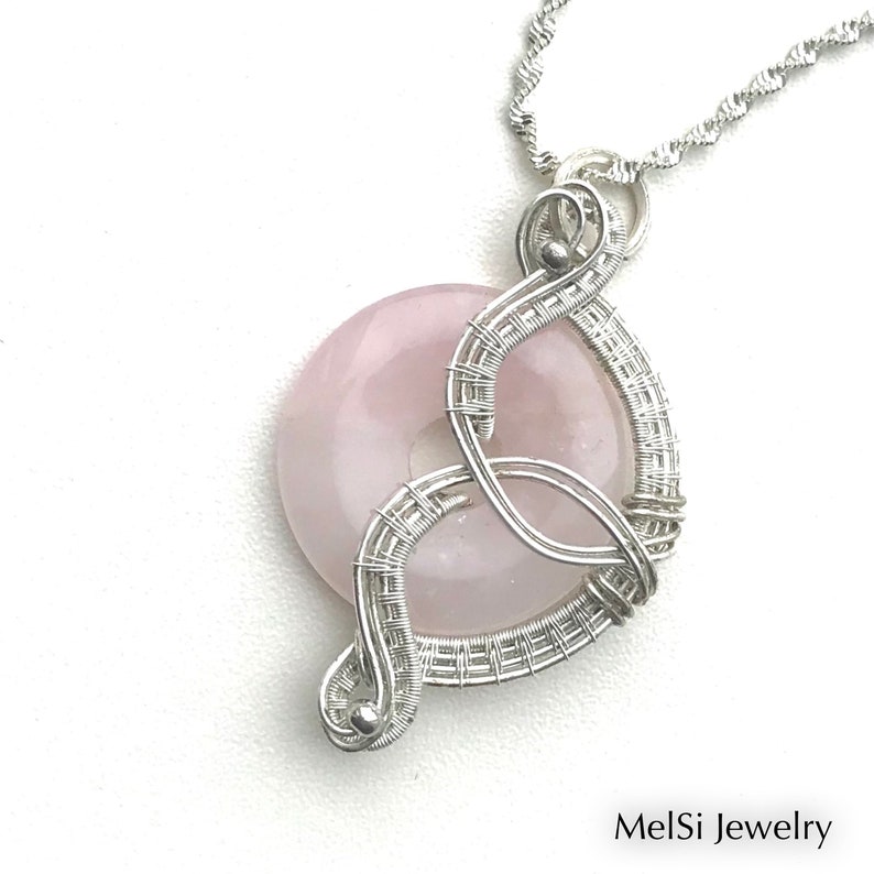 May include: A silver wire wrapped pendant featuring a pink rose quartz stone. The pendant is attached to a silver chain.