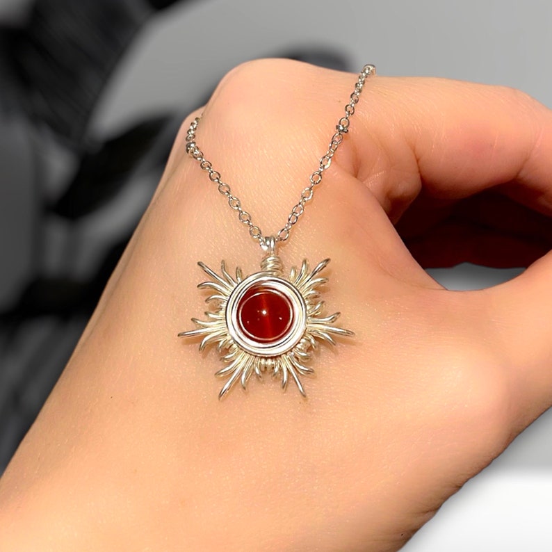 May include: A silver necklace with a red carnelian gemstone pendant in the shape of a sun.