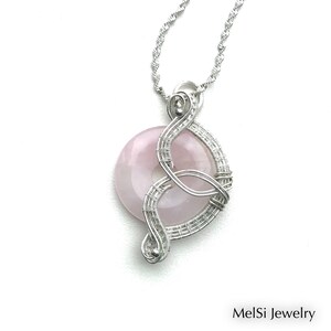 May include: A silver wire wrapped pendant featuring a pink gemstone. The pendant is attached to a silver chain.