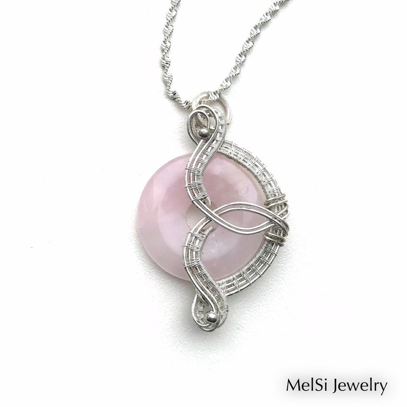 May include: A silver wire wrapped pendant featuring a round, pale pink gemstone. The pendant hangs from a silver chain.