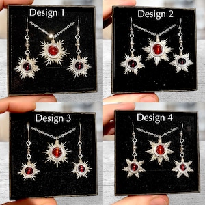 May include: Four designs of jewelry sets featuring a red gemstone sun pendant and matching earrings. Each set is displayed in a black box with the design number labeled on the top.