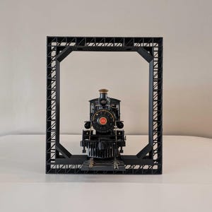 May include: A black toy train engine with a red number 808 on the front, positioned in a black metal frame.