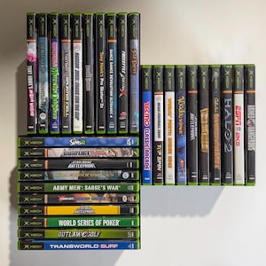May include: A collection of Xbox video game cases arranged in three groups. The titles include Tony Hawk's American Wasteland, Medal of Honor, Oddworld, Splinter Cell, NASCAR 2005, Haunted Mansion, Tony Hawk's Pro Skater 4, Dance Dance Revolution, and others.