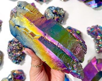 May include: A large iridescent crystal cluster displaying a rainbow of colours, including purple, blue, green, yellow, and orange. The crystal is a natural formation and has a unique, organic shape.