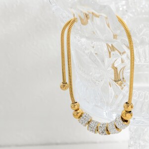 May include: A gold chain necklace with a series of round beads encrusted with clear rhinestones.
