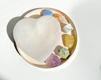 Peut inclure: Un bol en cristal de sélénite blanc en forme de cœur contenant une variété de cristaux, dont des cristaux bleus, jaunes, verts et blancs.