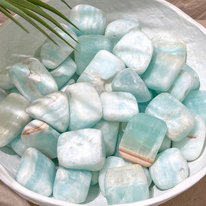 May include: A bowl filled with smooth, light blue and white tumbled stones. The stones have a natural, organic shape and a polished finish.