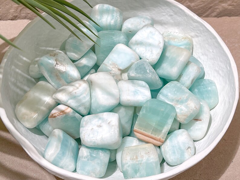 May include: A bowl filled with smooth, light blue and white tumbled stones. The stones have a natural, organic shape and a polished finish.