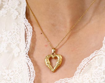 May include: A gold chain necklace with a heart-shaped pendant. The pendant has a detailed design of wings on either side of the heart.