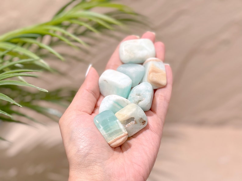 May include: A collection of smooth, light blue and white tumbled stones. The stones have a variety of shapes and sizes, and they are arranged in a hand.