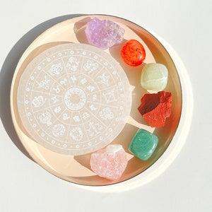 Peut inclure: Une roue zodiacale circulaire blanche avec les signes astrologiques gravés dessus, entourée de six cristaux colorés : une améthyste violette, une cornaline rouge, un jade vert, une aventurine vert clair, une rose quartz rose et un jaspe rouge.