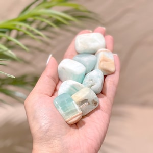 May include: A collection of smooth, light blue and white tumbled stones. The stones have a variety of shapes and sizes, and they are arranged in a hand.