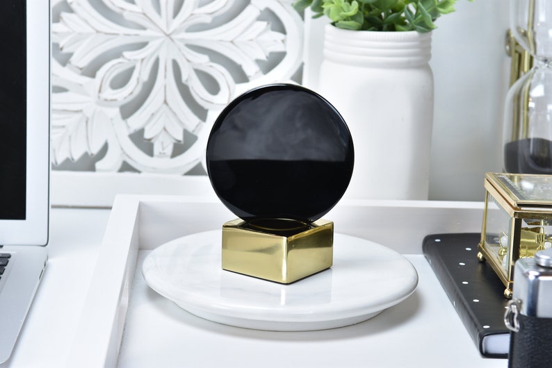 May include: A black and gold decorative object with a round black top and a square gold base. The object is sitting on a white plate.
