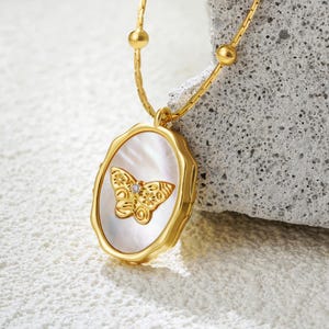 May include: A gold chain necklace with a white oval pendant featuring a gold butterfly with a small diamond accent.
