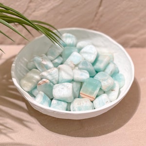 May include: A white bowl filled with light blue and white tumbled stones. The stones have a smooth, polished finish.