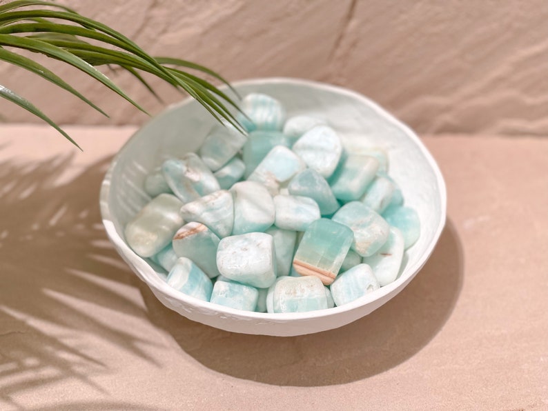 May include: A white bowl filled with light blue and white tumbled stones. The stones have a smooth, polished finish.