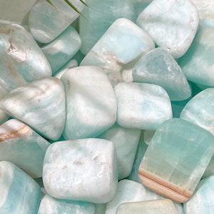 May include: A collection of tumbled blue and white caribbean calcite stones. The stones are smooth and polished, with a variety of shapes and sizes.