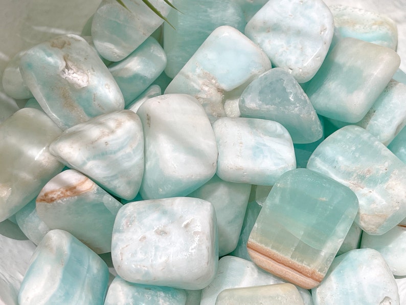 May include: A collection of tumbled blue and white caribbean calcite stones. The stones are smooth and polished, with a variety of shapes and sizes.