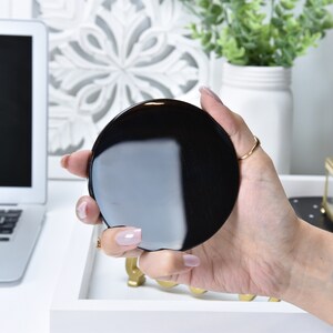 May include: A black round compact mirror with a reflective surface.
