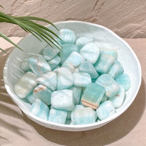 May include: A white bowl filled with light blue and white tumbled stones. The stones are smooth and have a natural, organic look.