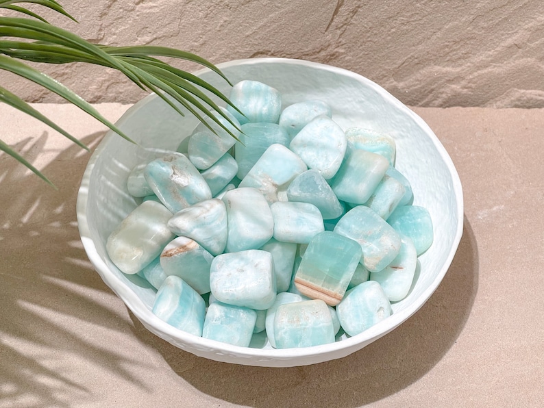May include: A white bowl filled with light blue and white tumbled stones. The stones are smooth and have a natural, organic look.