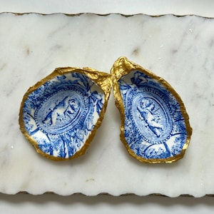 Pu&ograve; includere: Due conchiglie di ostriche in porcellana blu e bianca con finiture dorate. Ogni conchiglia presenta un design di cherubino.