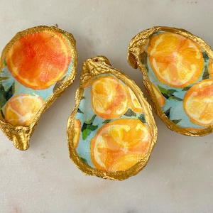 May include: Three gold oyster shell dishes with a blue and white citrus print. The shells are painted gold and have a glossy finish.