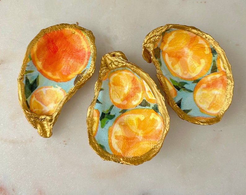 May include: Three gold oyster shell dishes with a blue and white citrus print. The shells are painted gold and have a glossy finish.